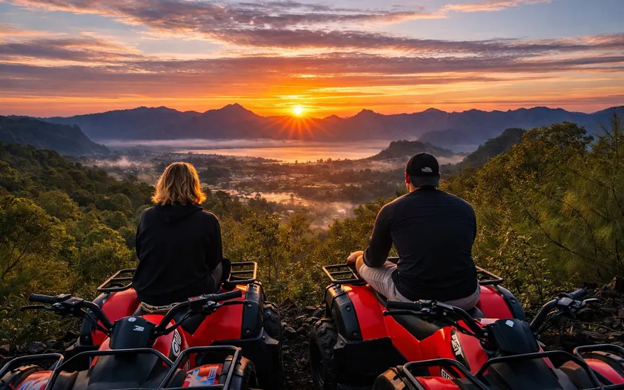 Two people on red quad bikes watching the sun come up over a misty valley