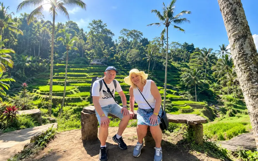 A couple sitting on a stone bench in front of green rice terraces and tall palms