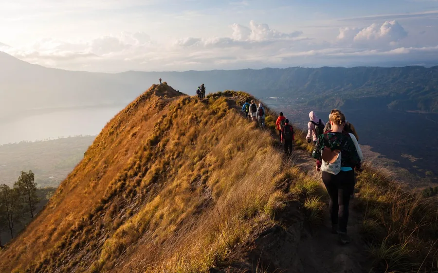 A line of walkers following a grassy ridge with the lake far below them